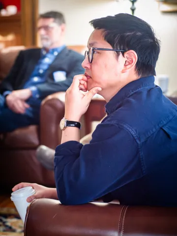 A scholar listening thoughtfully during a retreat session with coffee in hand.